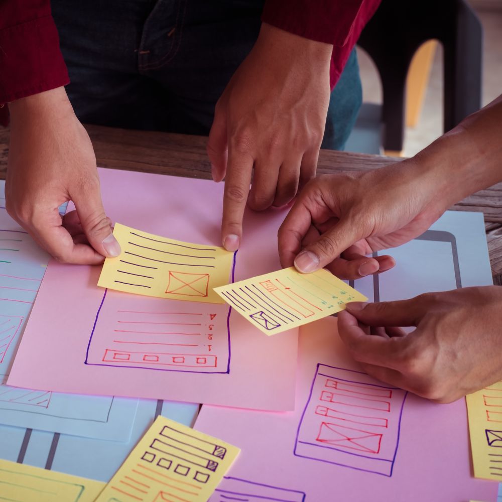 Trois mains collaborant sur des notes colorées et des plans, symbolisant la préparation méthodique pour une exposition réussie.