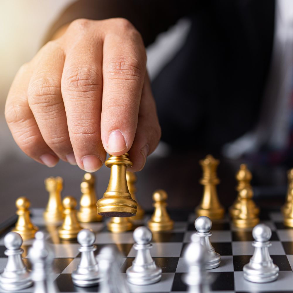 strategie-visiteurs-kiosque Main déplaçant une pièce d'échecs dorée, symbolisant des stratégies pour attirer des visiteurs à un kiosque d'exposition.